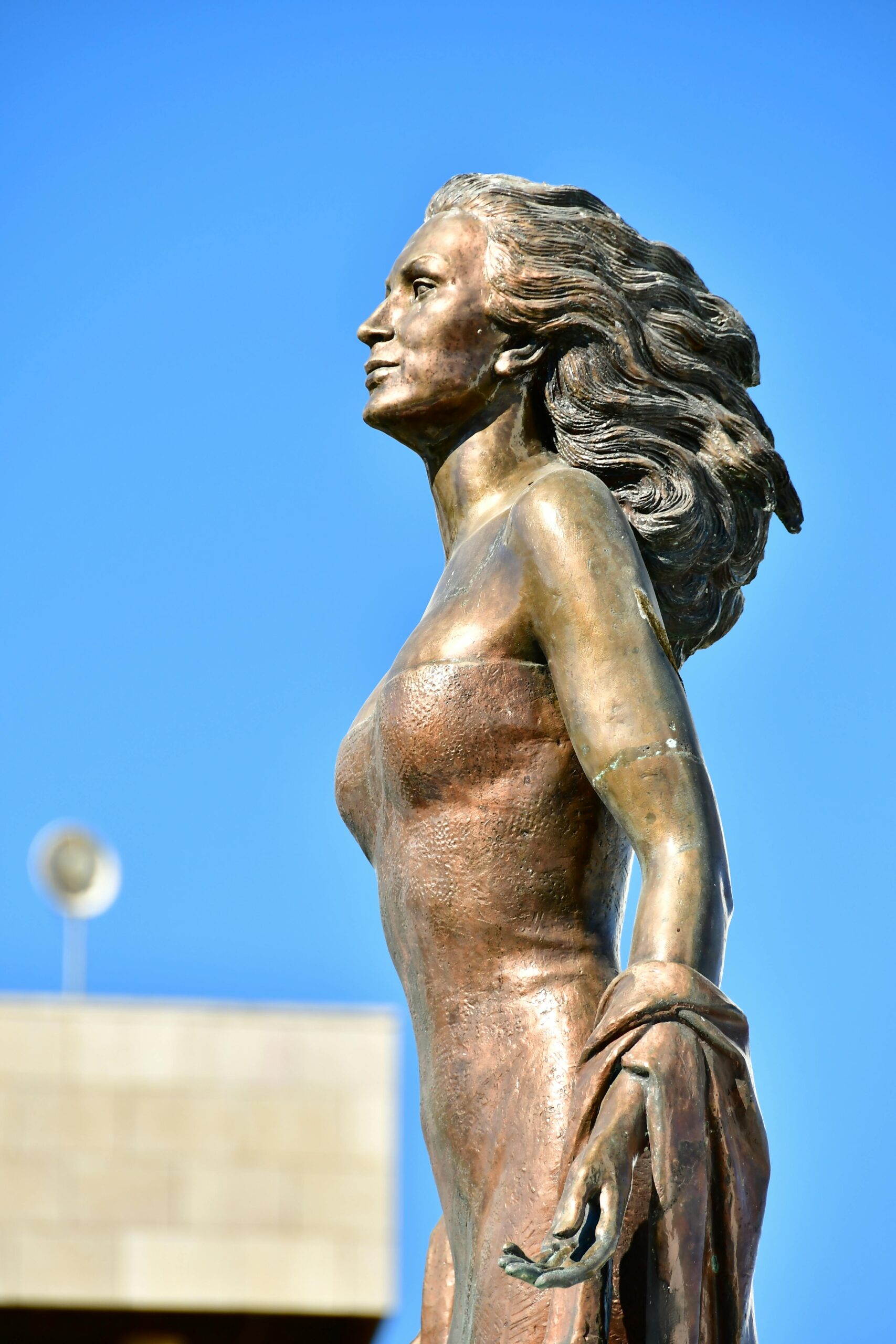 Elegant bronze statue of a woman with flowing hair against a vibrant blue sky.