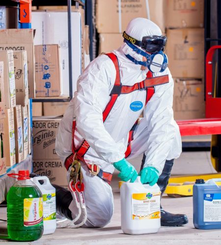 Industrial worker in protective gear handling chemicals in a warehouse environment.